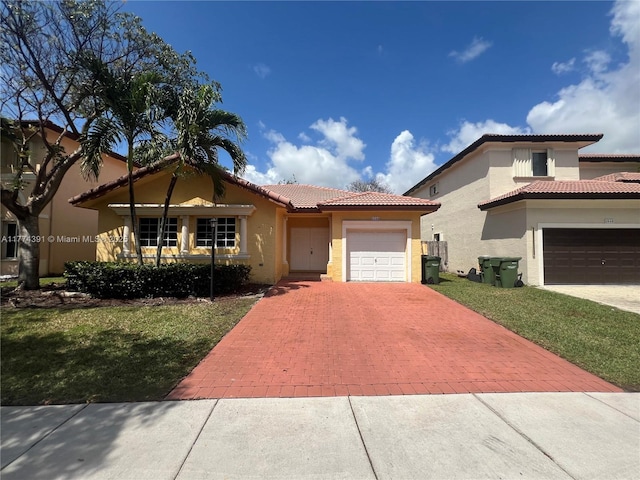mediterranean / spanish home featuring a tile roof, stucco siding, an attached garage, decorative driveway, and a front lawn