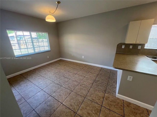 unfurnished dining area featuring baseboards, a sink, and a healthy amount of sunlight