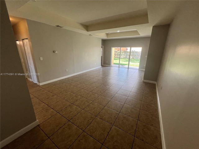 empty room with baseboards, a tray ceiling, and visible vents