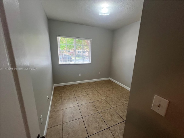 spare room with light tile patterned floors, baseboards, and a textured ceiling