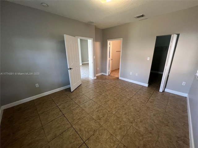 unfurnished bedroom with a closet, visible vents, baseboards, tile patterned floors, and a walk in closet