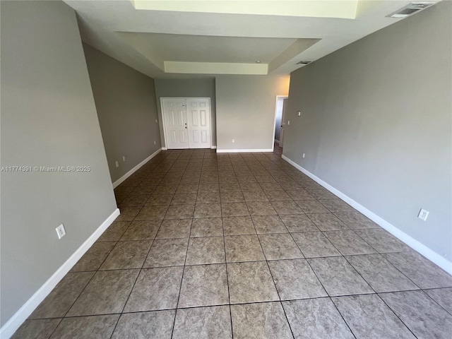 tiled empty room with baseboards, a tray ceiling, and visible vents
