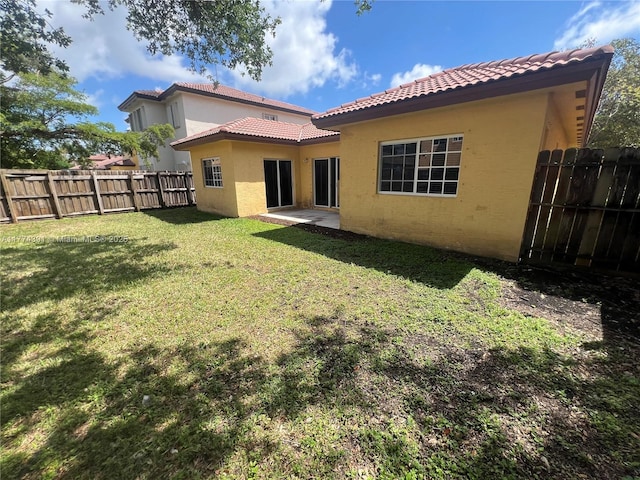 rear view of house with a tiled roof, a fenced backyard, stucco siding, a yard, and a patio area