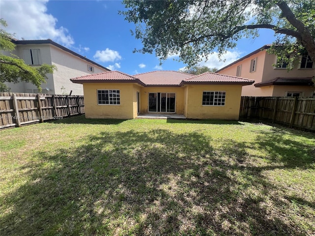 back of property with a fenced backyard, a tiled roof, stucco siding, and a yard