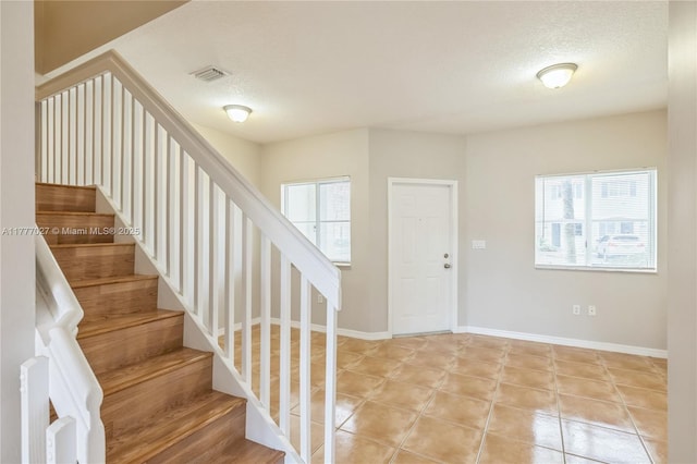 stairway with visible vents, baseboards, tile patterned floors, and a textured ceiling
