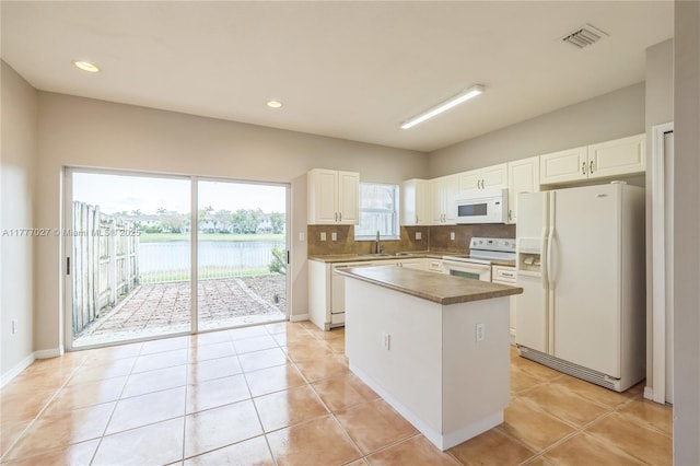 kitchen with a sink, a center island, white appliances, and white cabinets