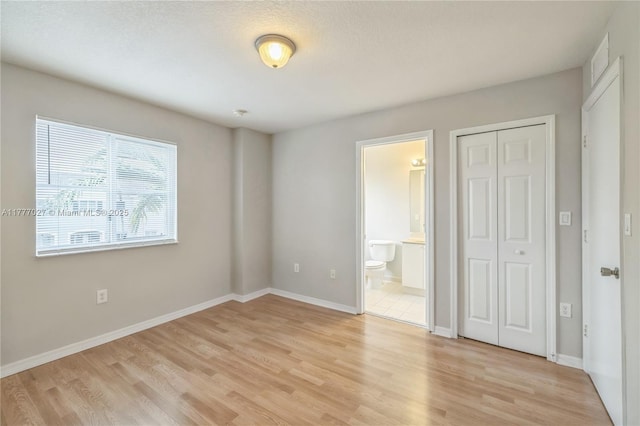 unfurnished bedroom with light wood finished floors, a closet, baseboards, and connected bathroom
