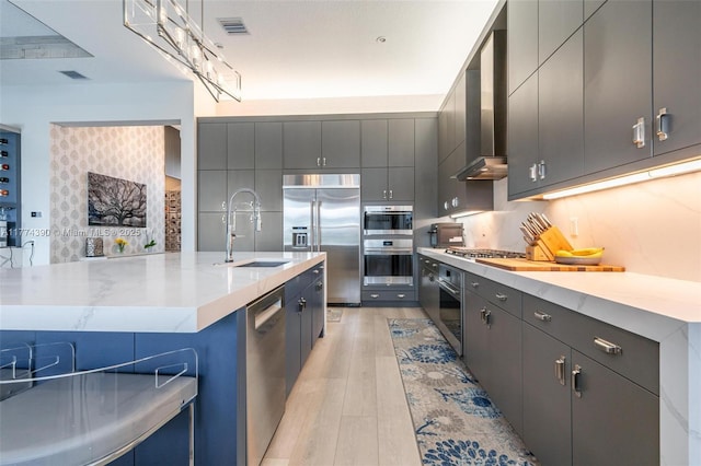 kitchen with a sink, appliances with stainless steel finishes, light wood-style flooring, wall chimney range hood, and visible vents