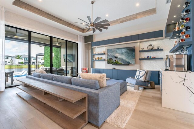 living area with ceiling fan, light wood-style floors, and a raised ceiling