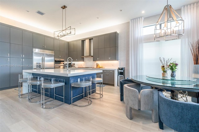 kitchen featuring gray cabinets, a sink, built in refrigerator, wall chimney range hood, and visible vents