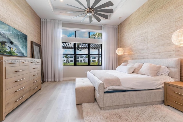 bedroom featuring a ceiling fan, wood finished floors, and a raised ceiling