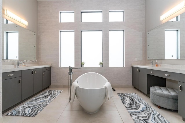 bathroom featuring a freestanding bath, a high ceiling, tile patterned flooring, and two vanities