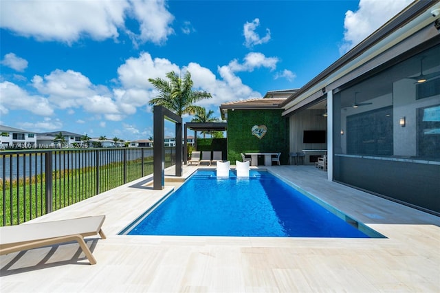 view of swimming pool featuring fence, a water view, a fenced in pool, a ceiling fan, and a patio area