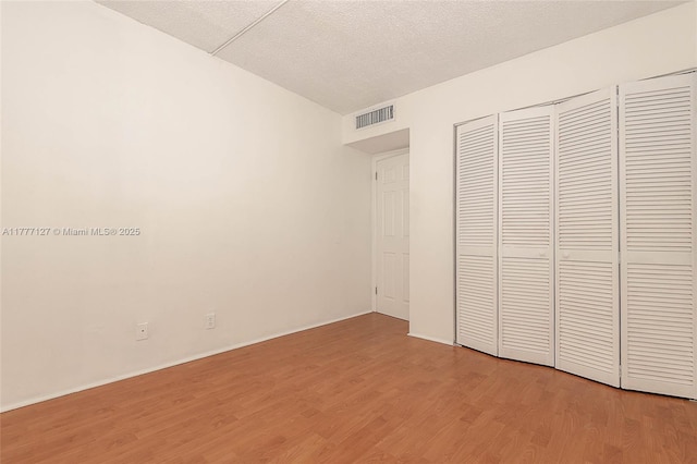 unfurnished bedroom featuring baseboards, a textured ceiling, light wood-style flooring, and visible vents