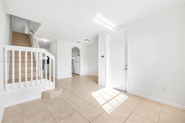 tiled empty room featuring arched walkways, baseboards, and stairway