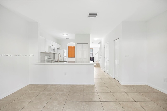 kitchen with light countertops, a sink, arched walkways, visible vents, and a peninsula