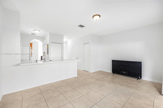 unfurnished living room with baseboards, visible vents, arched walkways, and a sink