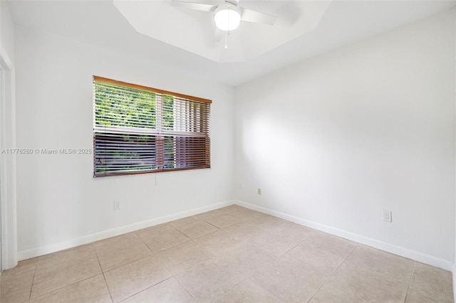 unfurnished room featuring tile patterned floors, a tray ceiling, baseboards, and ceiling fan