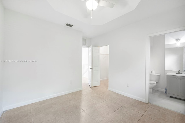 unfurnished bedroom featuring visible vents, baseboards, a sink, a tray ceiling, and a spacious closet