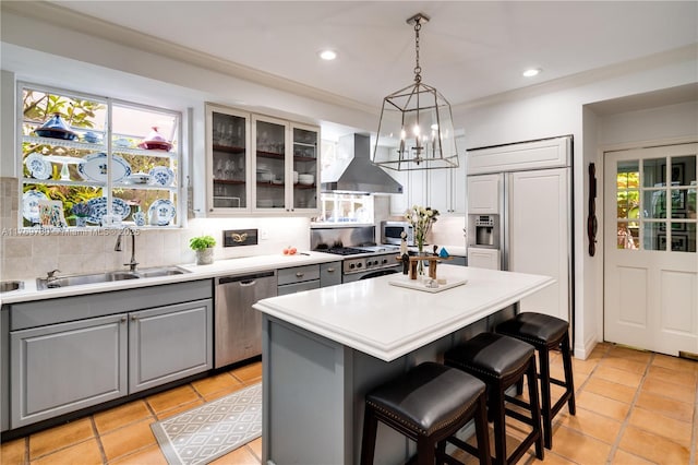 kitchen featuring wall chimney exhaust hood, stainless steel dishwasher, a sink, gray cabinetry, and backsplash