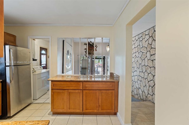 kitchen featuring light tile patterned floors, ornamental molding, freestanding refrigerator, washing machine and dryer, and brown cabinetry