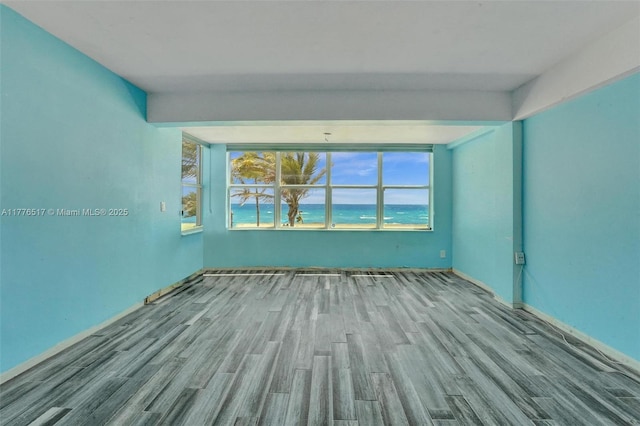 empty room featuring baseboards, wood finished floors, and a water view