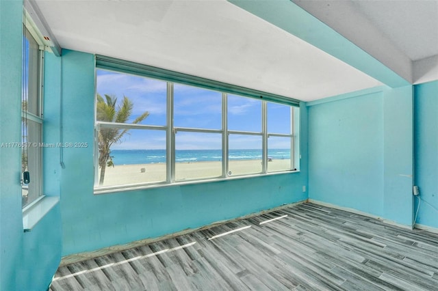spare room featuring a beach view, wood finished floors, and a water view