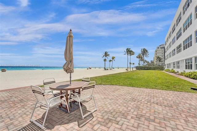 view of patio with a beach view, outdoor dining space, and a water view