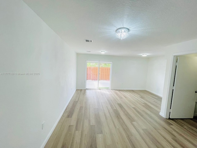 spare room featuring visible vents, baseboards, light wood-style floors, and a textured ceiling