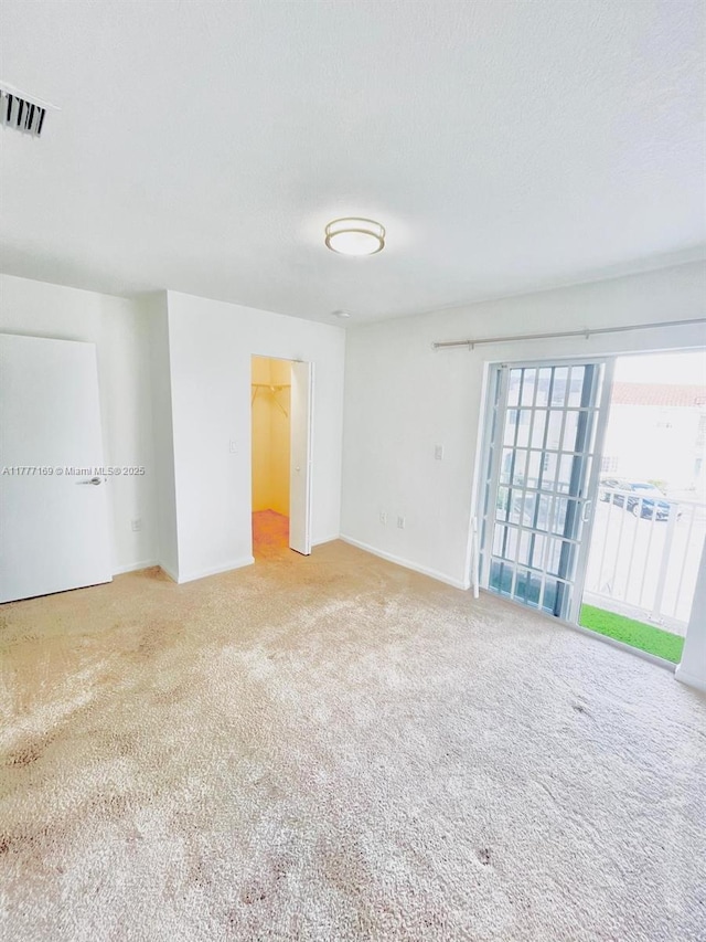 empty room with carpet flooring, a textured ceiling, baseboards, and visible vents
