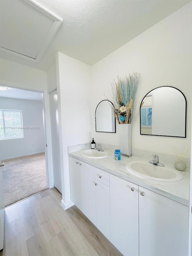 bathroom with double vanity, a textured ceiling, a sink, and wood finished floors