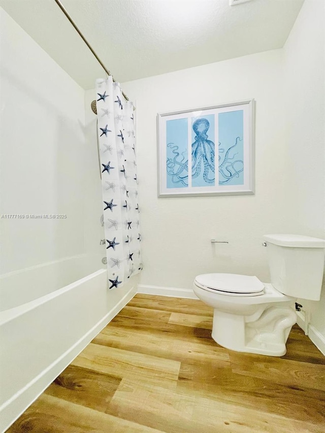 bathroom with toilet, wood finished floors, baseboards, and shower / bath combination with curtain