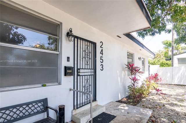 doorway to property featuring stucco siding and fence