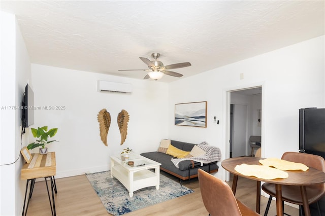 living area with light wood finished floors, a wall mounted air conditioner, ceiling fan, and baseboards