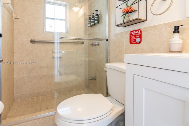 bathroom with tile walls, toilet, a shower stall, and vanity