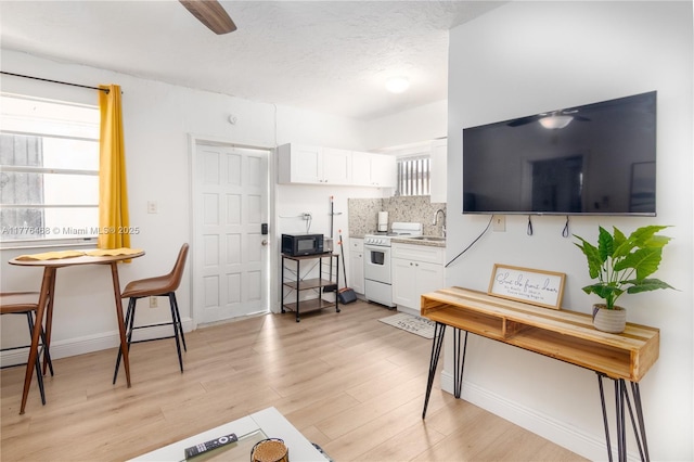 living area featuring a textured ceiling, baseboards, light wood finished floors, and a ceiling fan