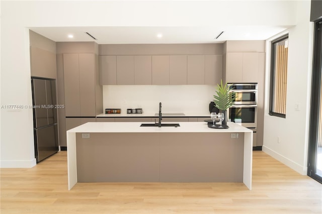 kitchen featuring light countertops, modern cabinets, appliances with stainless steel finishes, a sink, and light wood-type flooring