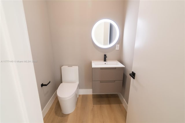 half bath featuring toilet, vanity, baseboards, and wood finished floors