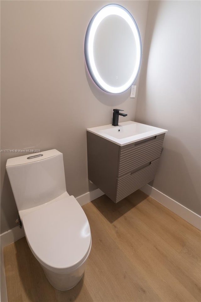 bathroom with toilet, vanity, baseboards, and wood finished floors