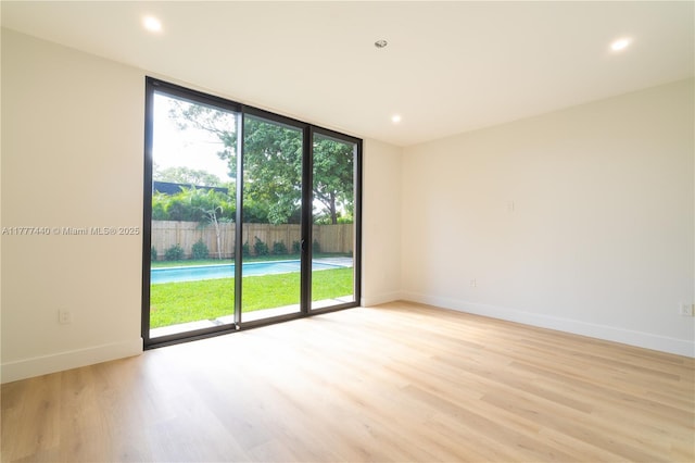 spare room with recessed lighting, baseboards, light wood-style floors, and a wall of windows