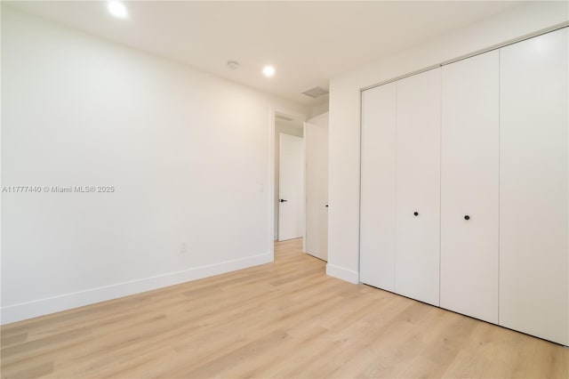 unfurnished bedroom featuring a closet, baseboards, light wood-style floors, and recessed lighting