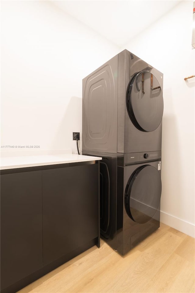 laundry room with stacked washer / dryer, baseboards, light wood-style floors, and laundry area