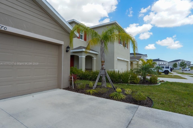 view of front of home with stucco siding, concrete driveway, a front yard, and a residential view