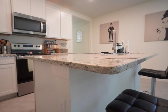 kitchen with a kitchen island, white cabinetry, light stone countertops, a breakfast bar, and stainless steel appliances