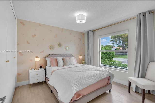 bedroom featuring baseboards, light wood-style floors, a textured ceiling, and wallpapered walls
