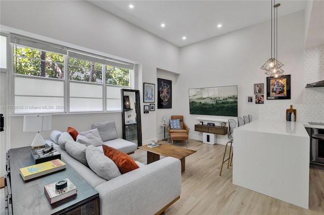 living area featuring baseboards, a high ceiling, light wood finished floors, and recessed lighting