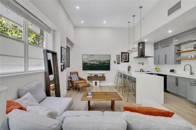 living room with a high ceiling, indoor wet bar, visible vents, and light wood-type flooring