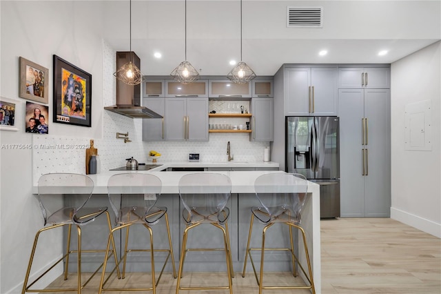 kitchen featuring wall chimney range hood, a peninsula, stainless steel refrigerator with ice dispenser, gray cabinetry, and visible vents