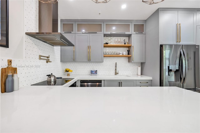 kitchen with stainless steel appliances, backsplash, wall chimney range hood, gray cabinets, and a sink