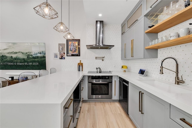 kitchen featuring a sink, black appliances, a peninsula, light countertops, and wall chimney exhaust hood